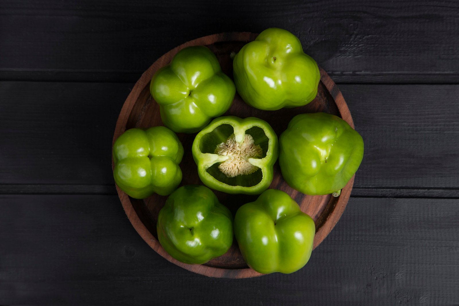 Whole and sliced green bell peppers placed on wooden dark table
